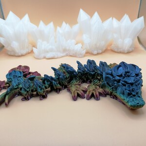 May include: The image showcases two distinct 3D-printed art pieces. The top features a series of white, crystalline structures. Below, a detailed, multi-colored dragon sculpture is displayed, with hues of blue, green, and purple.
