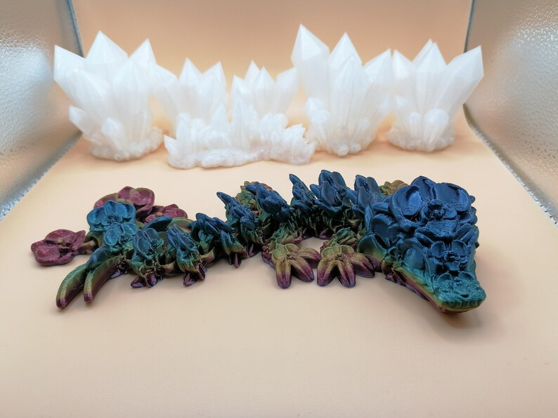 May include: The image showcases two distinct 3D-printed art pieces. The top features a series of white, crystalline structures. Below, a detailed, multi-colored dragon sculpture is displayed, with hues of blue, green, and purple.