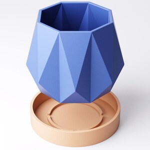 May include: A geometric, blue planter with a matching peach-coloured saucer. The planter has a faceted design, creating a modern and stylish look. This decorative piece is suitable for indoor plants and adds a pop of colour to any room.