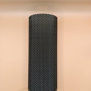 K&ouml;nnte beinhalten: Eine zylindrische schwarze Lampe mit einem strukturierten, gewebten Muster. Die Lampe hat einen wei&szlig;en Sockel und einen schwarzen Rand. Ein wei&szlig;es Kabel erstreckt sich von der Basis. Der Hintergrund ist einfarbig pfirsichfarben.