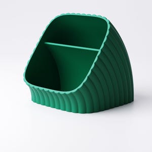 May include: A green desk tidy with a scalloped edge and vertical ribbed detailing. The organiser has two compartments, suitable for storing pens, pencils, or other office supplies. The design is modern and minimalist, suitable for any workspace.