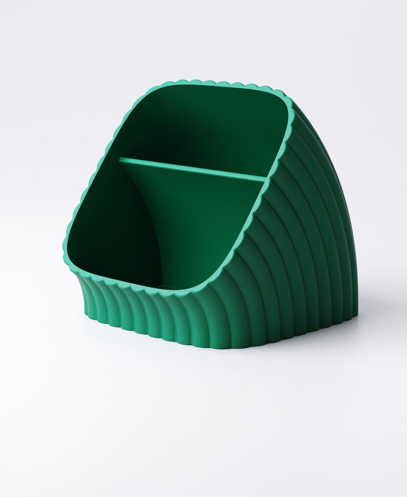 May include: A green desk tidy with a scalloped edge and vertical ribbed detailing. The organiser has two compartments, suitable for storing pens, pencils, or other office supplies. The design is modern and minimalist, suitable for any workspace.