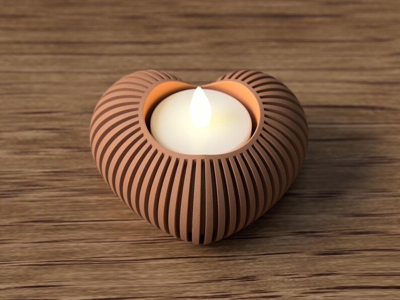 May include: A heart-shaped candle holder with a warm, glowing candle inside. The holder is made of a light brown material with vertical grooves, creating a textured effect. The candle holder sits on a wooden surface.