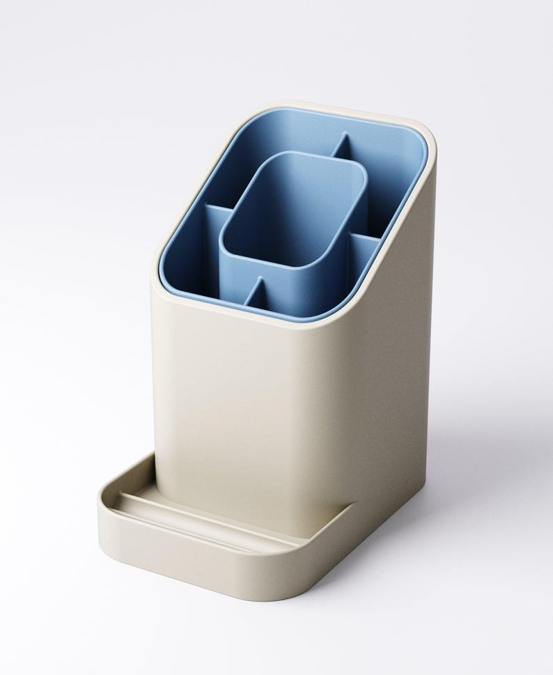 May include: A beige and blue desk organizer with multiple compartments. The organizer has a rectangular base with a small tray at the bottom. The interior is blue, with a central rectangular section and several smaller compartments. The exterior is a neutral beige color.