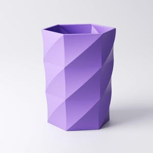 May include: A lavender-colored, geometric pen holder with a faceted design. The hexagonal base transitions into a cylindrical shape with diagonal, textured panels. The interior is divided into sections.