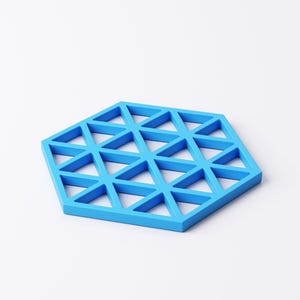 Pu&ograve; includere: Un sottobicchiere blu brillante a forma esagonale con un design geometrico. Il sottobicchiere presenta un motivo triangolare ripetuto. &Egrave; realizzato in un materiale solido e si trova su uno sfondo bianco. Circa 15 cm di diametro.