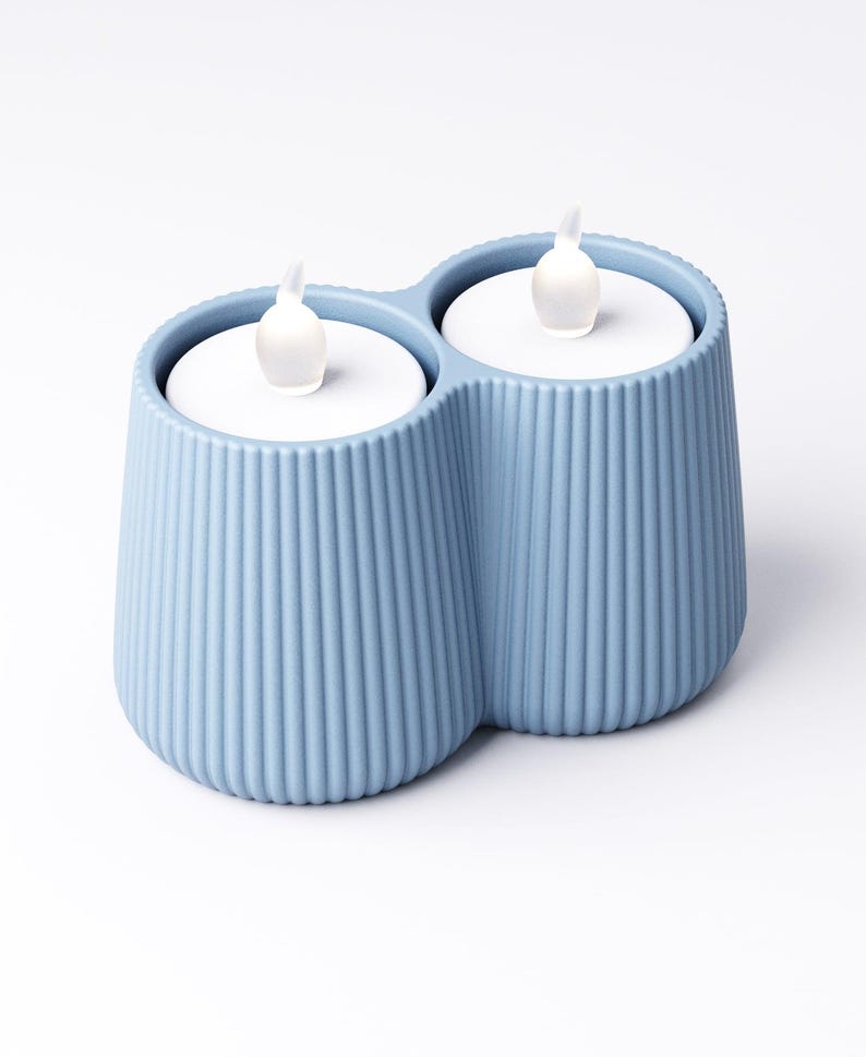 May include: A light blue, double-cup candle holder with two white LED candles. The holder has a ribbed texture and a modern design. The candles have a realistic flame effect, creating a warm and inviting ambiance.