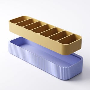 May include: A two-piece organizer set. The top section is mustard yellow with six compartments. The bottom section is lavender with vertical ribbed detailing. The organizer is designed for desk or drawer organization.