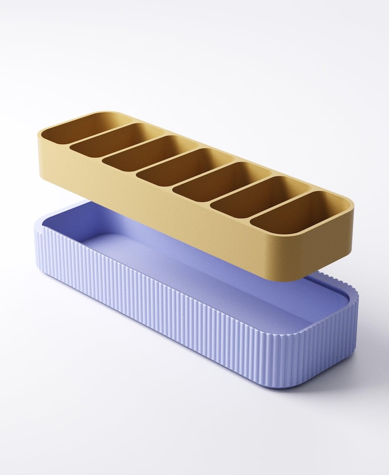 May include: A two-piece organizer set. The top section is mustard yellow with six compartments. The bottom section is lavender with vertical ribbed detailing. The organizer is designed for desk or drawer organization.