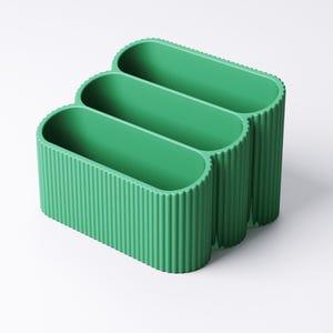 May include: A three-section, green desk organizer with a ribbed exterior. The organizer has an oval shape and is made of a solid, opaque material. The sections are open at the top for easy access.