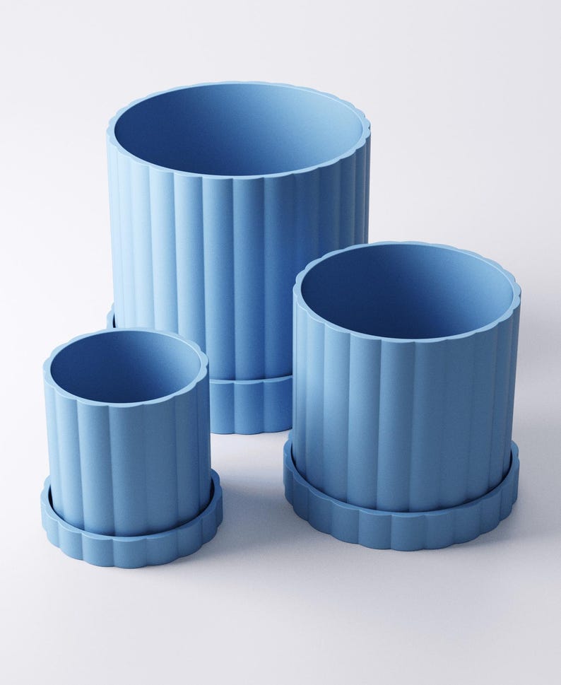May include: Three light blue cylindrical planters of varying sizes. Each planter has vertical ridged detailing and sits on a matching, scalloped-edge saucer. The planters are arranged on a white surface.