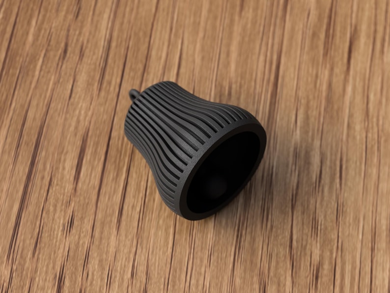 May include: A black, bell-shaped object with a ridged exterior and a small loop at the top. The interior is a smooth, dark surface. The object is set against a wooden background.