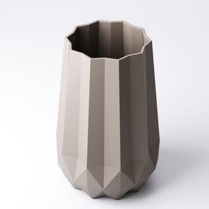 K&ouml;nnte beinhalten: Eine taupefarbene Vase mit geometrischem, facettiertem Design. Die Vase hat eine breite, unregelm&auml;&szlig;ige Oberseite und einen sich verj&uuml;ngenden, eckigen K&ouml;rper. Die neutrale Farbe und die moderne Form machen sie zu einem vielseitigen Dekorationsartikel.
