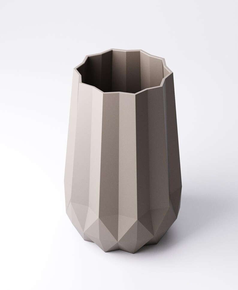 K&ouml;nnte beinhalten: Eine taupefarbene Vase mit geometrischem, facettiertem Design. Die Vase hat eine breite, unregelm&auml;&szlig;ige Oberseite und einen sich verj&uuml;ngenden, eckigen K&ouml;rper. Die neutrale Farbe und die moderne Form machen sie zu einem vielseitigen Dekorationsartikel.