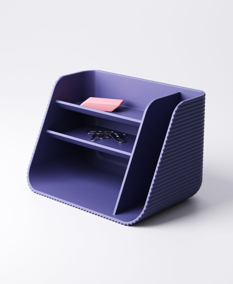 May include: A purple desk organizer with two shelves and a ribbed side. A pink eraser and silver paper clips rest on the shelves. The organizer is made of a solid material and has a modern design.