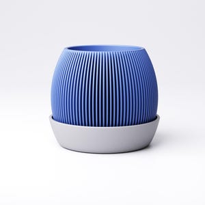 May include: A blue, ribbed, cylindrical planter with a matching gray saucer. The planter has vertical lines and a rounded shape. The saucer is a simple, low-profile design. The overall aesthetic is modern and minimalist.
