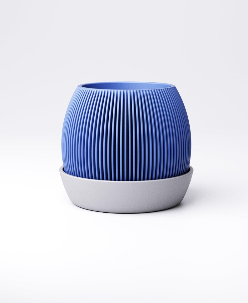 May include: A blue, ribbed, cylindrical planter with a matching gray saucer. The planter has vertical lines and a rounded shape. The saucer is a simple, low-profile design. The overall aesthetic is modern and minimalist.