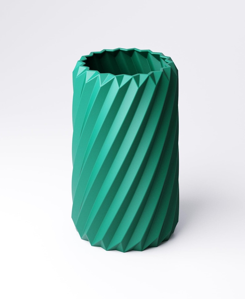 May include: A teal-colored, cylindrical vase with a geometric, ridged design. The vase has a twisted, spiral appearance, with a jagged edge at the top. The vase is made of a solid material and is suitable for home decor.