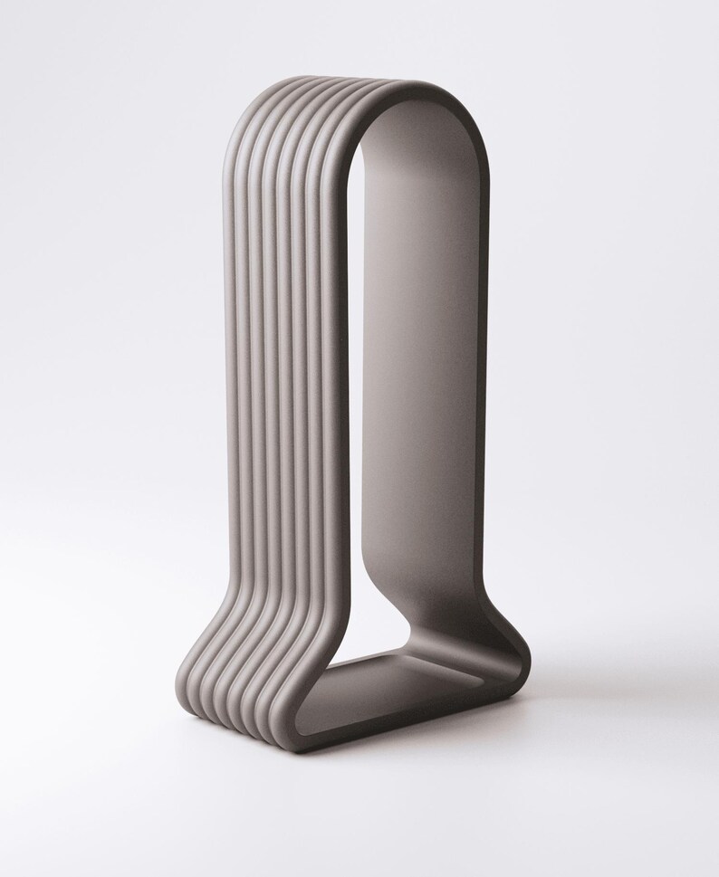 May include: A modern, minimalist sculpture in a muted gray color. The design features a curved, U-shaped form with vertical, ridged lines on one side, creating a textured effect. The sculpture stands on a flat base.