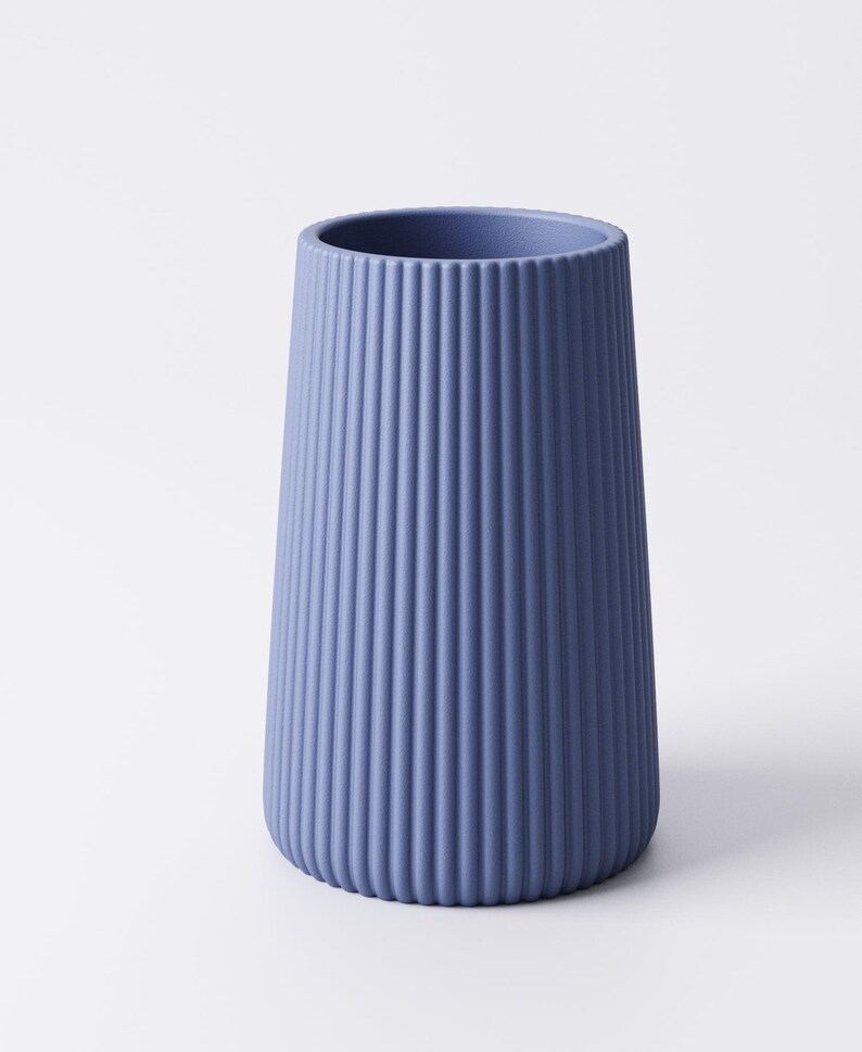 May include: A blue vase with a ribbed exterior. The vase has a cylindrical shape that tapers slightly towards the base. The color is a muted blue, and the surface has vertical ridges. The vase is likely made of ceramic or a similar material.