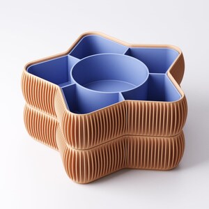 May include: A star-shaped storage container with a light brown exterior and a blue interior. The container is divided into multiple compartments, including a central circular section. The exterior has a ribbed design.