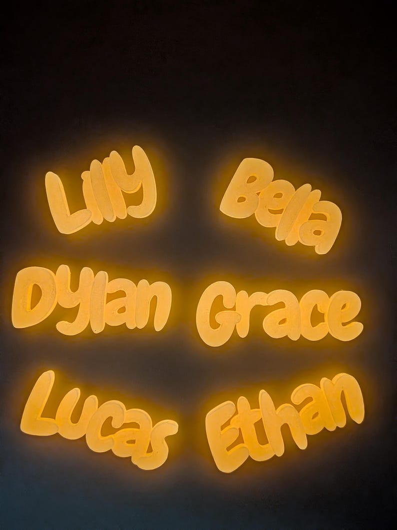 May include: Illuminated name signs in a warm yellow colour. The names "Lilly", "Bella", "Dylan", "Grace", "Lucas", and "Ethan" are presented in a playful, rounded font, ideal for nursery or bedroom decoration.