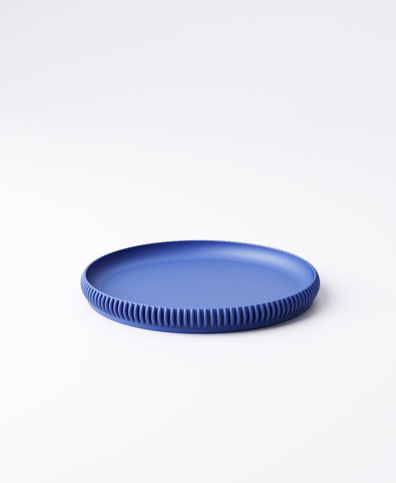 May include: A round, cobalt blue plate with a ribbed edge. The plate is made of a solid material and sits on a white background. The plate's design is simple and modern, suitable for serving food.