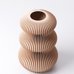 Peut inclure: Un vase beige &agrave; trois niveaux avec un design nervur&eacute; unique. Le vase a une large ouverture en haut et une s&eacute;rie de lignes verticales incurv&eacute;es qui cr&eacute;ent une surface textur&eacute;e. Le vase est un objet d&eacute;coratif.