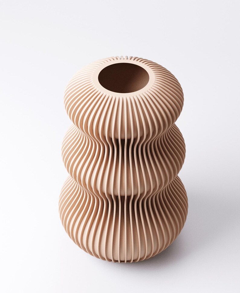 Peut inclure: Un vase beige &agrave; trois niveaux avec un design nervur&eacute; unique. Le vase a une large ouverture en haut et une s&eacute;rie de lignes verticales incurv&eacute;es qui cr&eacute;ent une surface textur&eacute;e. Le vase est un objet d&eacute;coratif.
