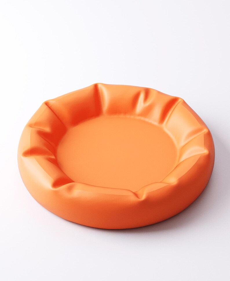 May include: A round, orange tray with a slightly raised, pleated edge. The tray has a smooth, matte finish and a shallow interior. The design is simple and modern, suitable for serving or display.