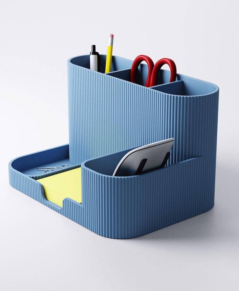 May include: A blue desk tidy with various compartments. It includes sections for pens, pencils, and scissors, a tray for sticky notes and a slot for a tablet. The organiser is made of a ribbed material.