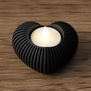 May include: A black heart-shaped candle holder with a glowing white candle. The holder has a ribbed design and is made of a dark material. The candle holder is on a wooden surface.