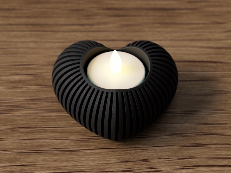 May include: A black heart-shaped candle holder with a glowing white candle. The holder has a ribbed design and is made of a dark material. The candle holder is on a wooden surface.