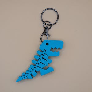May include: A blue dinosaur skeleton keychain with a black metal clasp and keyring. The dinosaur skeleton is made of a segmented material, with a detailed rib cage, spine, and head. The keychain is a fun accessory.