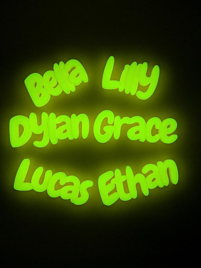 May include: A dark background highlights glowing green names: "Bella," "Lilly," "Dylan Grace," "Lucas," and "Ethan." The names are written in a bright, neon-like font, giving off a vibrant, luminous effect.