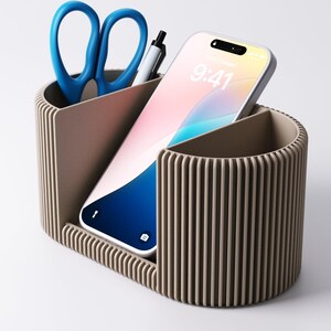 May include: A taupe desk tidy with three sections. One contains blue scissors and a pen, another a smartphone showing 9:41, and the third is empty. The organiser has a ribbed design.