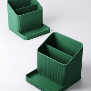 May include: Two green desk organizers with a ribbed texture. Each organizer has two compartments and a small tray. The organizers are made of a solid green material and are designed to hold pens, pencils, and other office supplies.