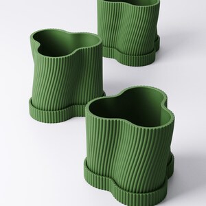 May include: Three green plant pots with a wavy top edge and a ridged, vertical design. Each pot sits on a matching, scalloped base. The pots are arranged on a white background.