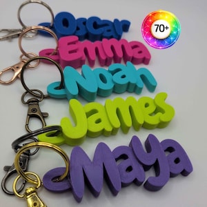 May include: A collection of five 3D-printed name keychains in blue, pink, teal, lime green, and purple. Each keychain features a name&mdash;Oscar, Emma, Noah, James, or Maya&mdash;attached to a metal split ring and a lobster clasp. A circular icon displays 70+.