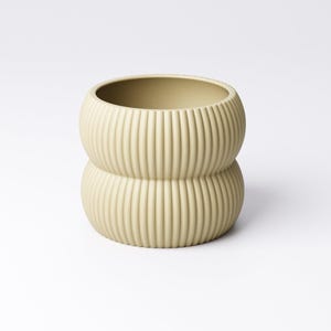 May include: A light green, ribbed ceramic vase with a stacked, rounded design. The vase has a wide opening and a textured surface with vertical lines. The neutral color and unique shape make it a decorative item for any room.