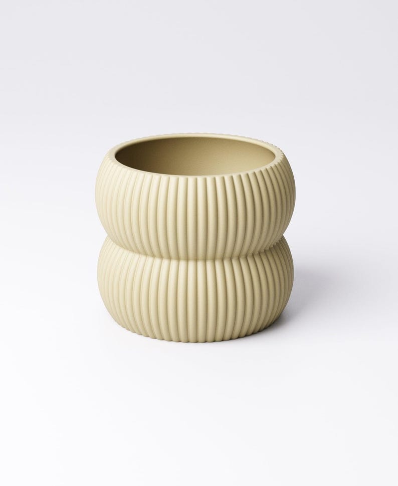 May include: A light green, ribbed ceramic vase with a stacked, rounded design. The vase has a wide opening and a textured surface with vertical lines. The neutral color and unique shape make it a decorative item for any room.
