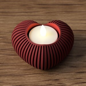 May include: A heart-shaped candle holder in a deep red hue, featuring a slotted design. The holder cradles a glowing white candle, creating a warm ambiance. The candle holder is placed on a wooden surface.