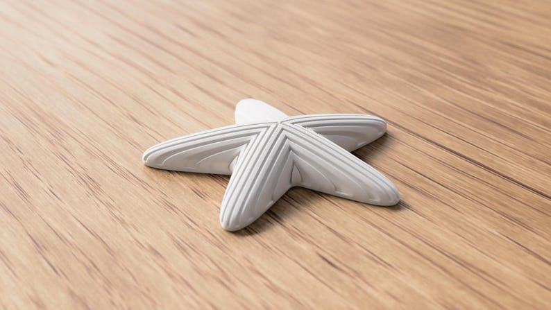 May include: A white, five-pointed starfish-shaped decorative object with ridged detailing. The object is resting on a light brown wooden surface, creating a contrast in textures and colors. The starfish design is a common theme in coastal decor.