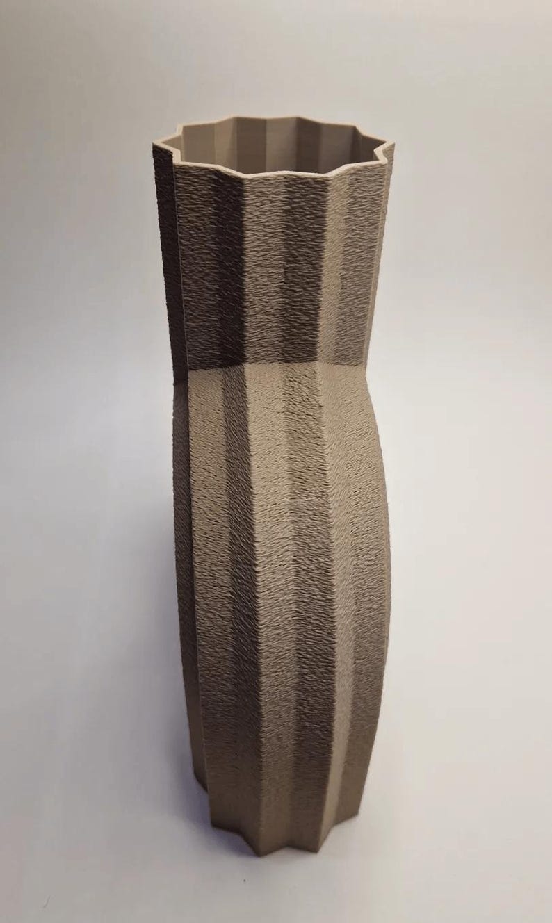 May include: A tall, textured vase in shades of brown and tan. The vase has a unique, geometric design with vertical ridges and a star-shaped top. The vase is approximately 12 inches tall.