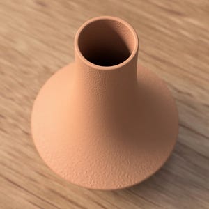 May include: A peach-colored ceramic vase with a round base and a narrow neck. The vase has a textured surface and sits on a wooden surface. The vase is empty and ready to be filled with flowers or other decorative items.