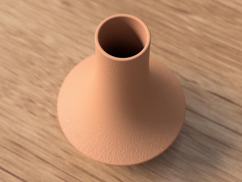 May include: A peach-colored ceramic vase with a round base and a narrow neck. The vase has a textured surface and sits on a wooden surface. The vase is empty and ready to be filled with flowers or other decorative items.