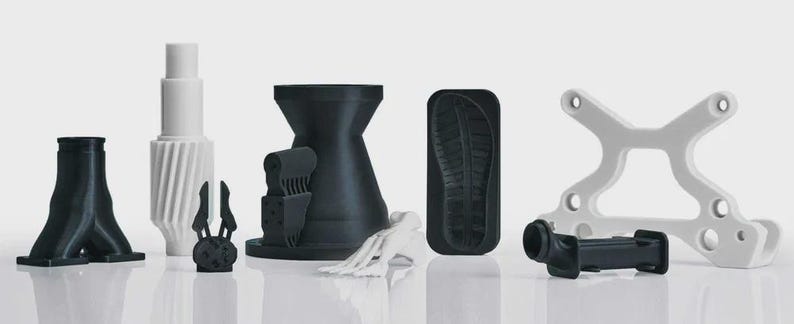 May include: A collection of 3D-printed objects in black and white. The objects include a Y-shaped structure, a cylindrical piece with a spiral design, a claw-like shape, a shoe sole imprint, and a cross-shaped frame. The objects are displayed on a reflective surface.