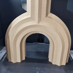 May include: A beige, 3D-printed architectural model with an arched design. The model has a textured surface and is made of PLA plastic. The structure is placed on a black surface, likely a 3D printer bed.