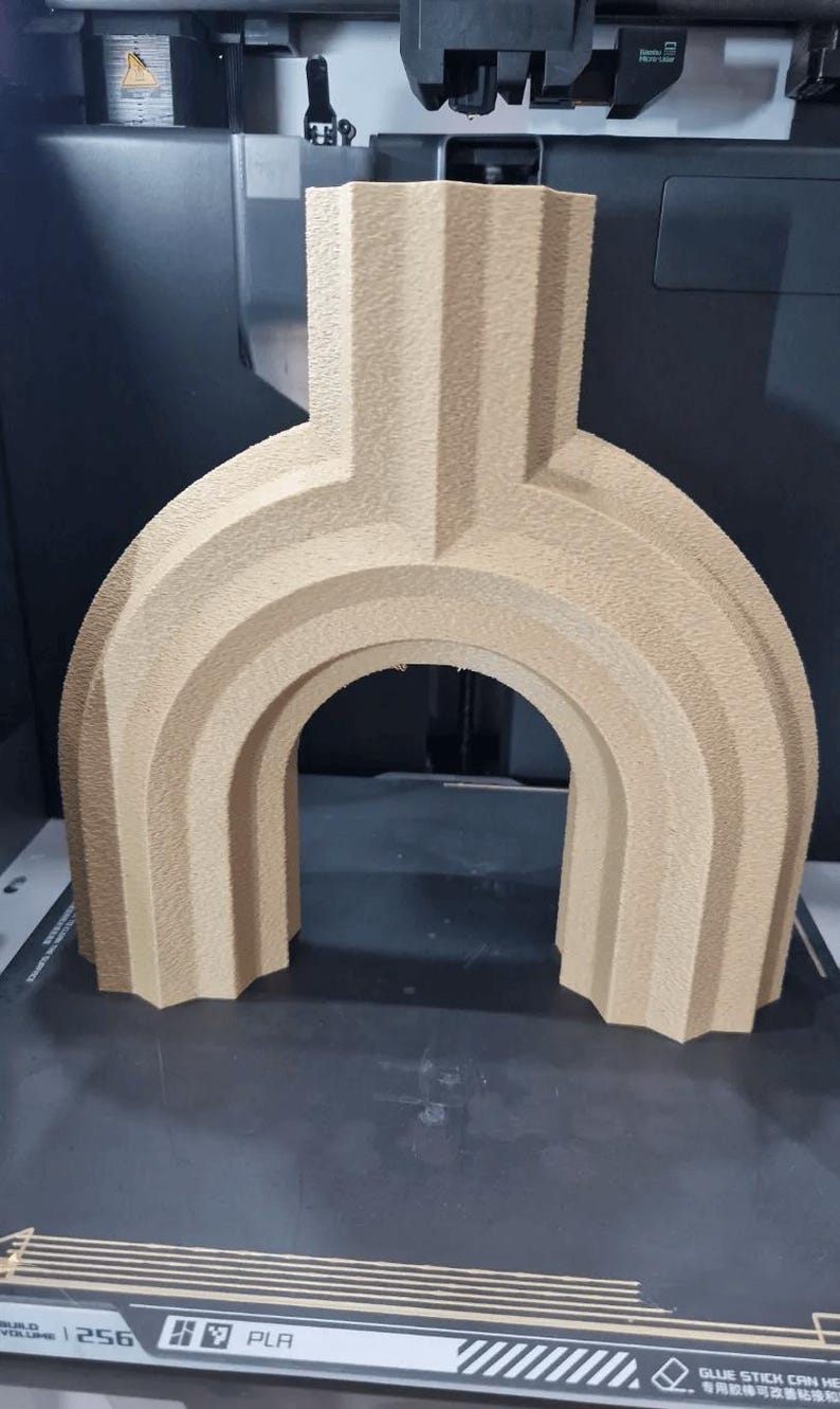 May include: A beige, 3D-printed architectural model with an arched design. The model has a textured surface and is made of PLA plastic. The structure is placed on a black surface, likely a 3D printer bed.