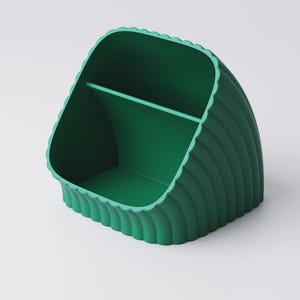 May include: A green desk tidy with a scalloped edge design. The organiser has a curved shape with a divider inside, creating two compartments. The exterior features vertical ridges, adding texture. The colour is a vibrant, solid green.